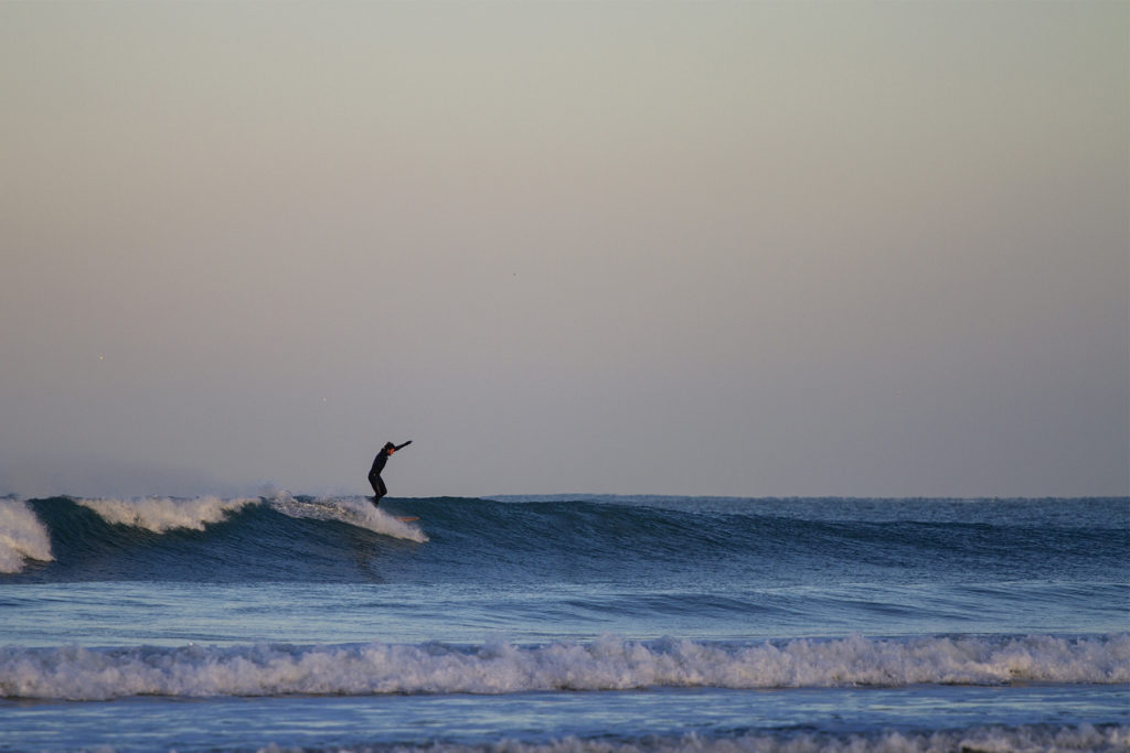 Chris runs to the nose arms up on the Otter Surfboards wooden longboard Seasaw at Godrevy