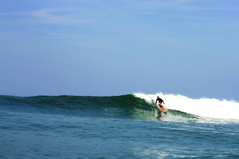 James Otter drops into a wave on the Pier wooden surfboard at Chapel Porth, Cornwall in summer. Riz Boardshorts