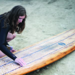 Rebecca Pepperell waxing the Otter Surfboards Seasaw wooden longboard at Perranporth in Cornwall