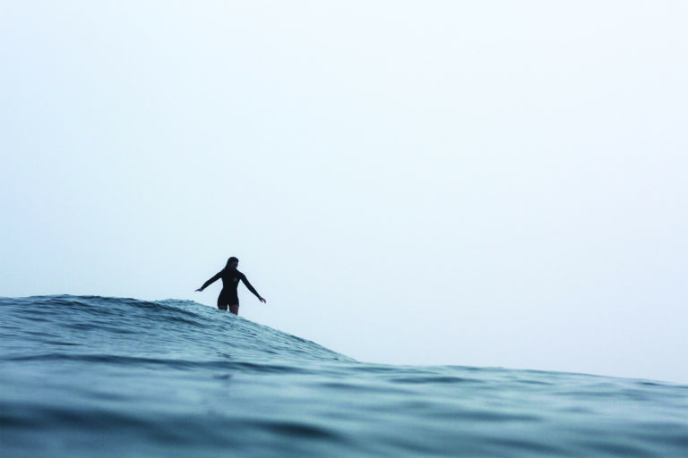 Becky gliding along a wave in the mist on the Otter Surfboards wooden Seasaw model