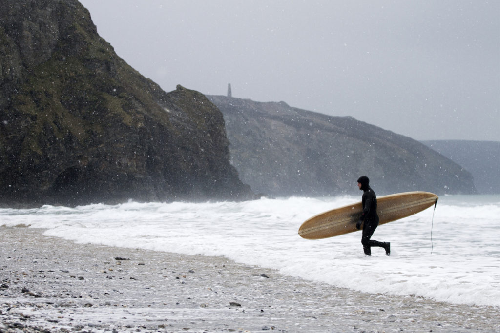 Otter Wooden Surfboard being carried out of the surf at Porthtowan in the snow. Wicket