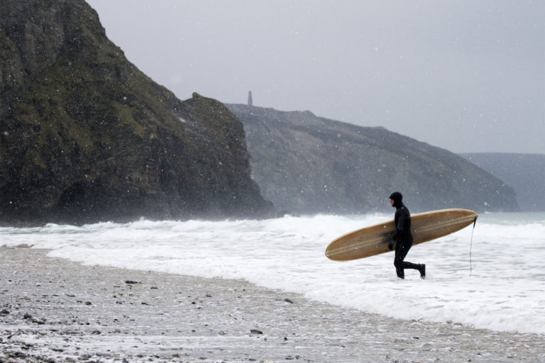 Otter Wooden Surfboard being carried out of the surf at Porthtowan in the snow. Wicket