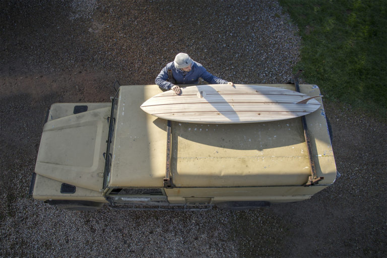 James Otter with a Wooden surfboard on top of a Landrover Defender. Clipper