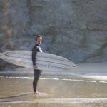 James Otter portrait, standing on the beach at porthtowan with his Clipper wooden surfboard.