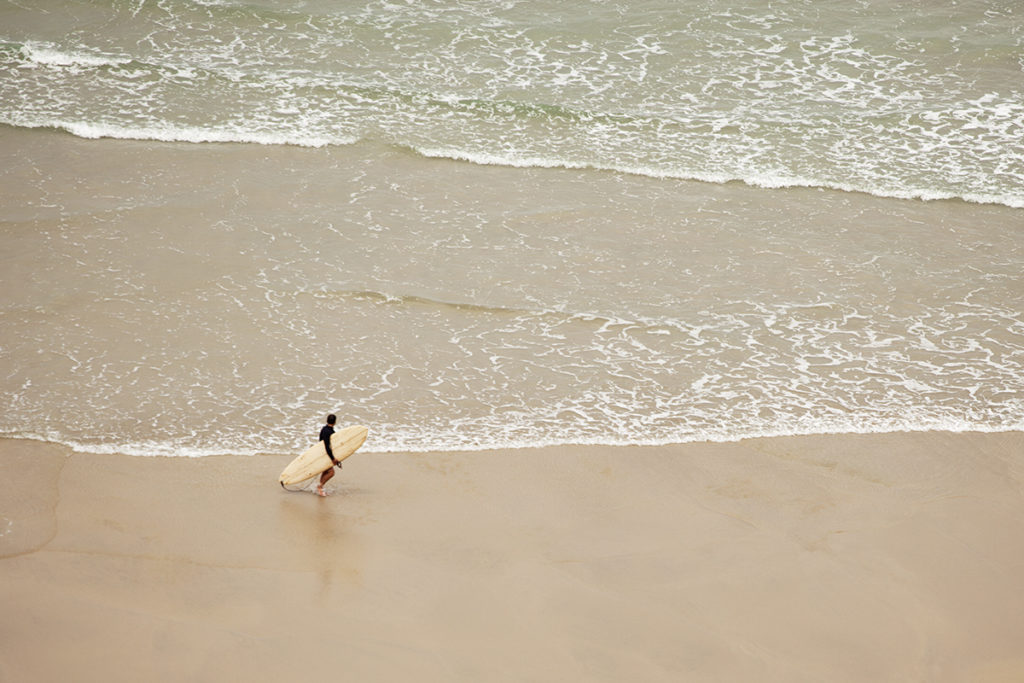 Marcus exits the surf with the Otter Surfboards Wooden Coaster at Chapel Porth, Cornwall. sandy beach