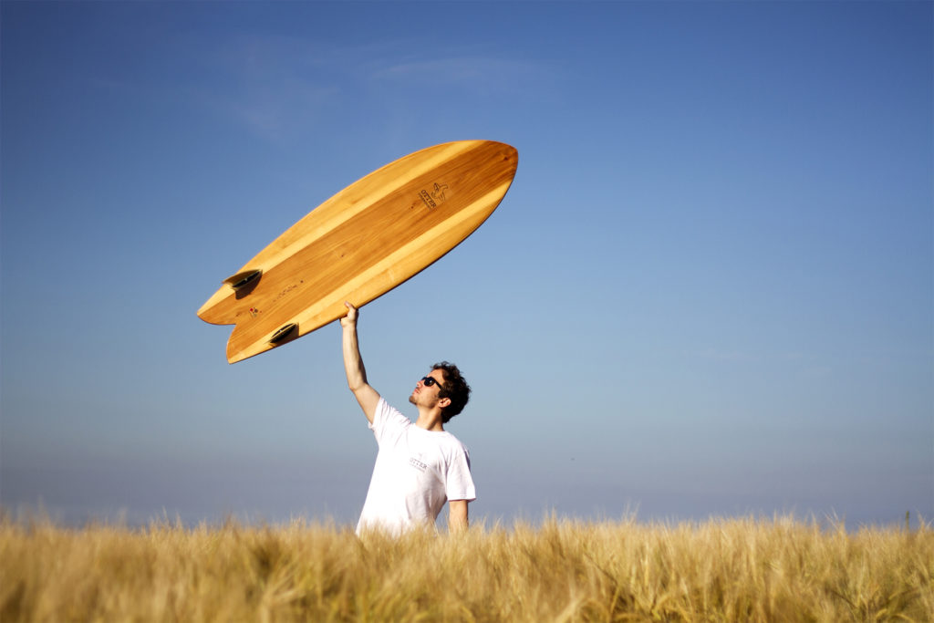 wooden surfboard fish held overhead in a corn field otter surfboards fetch