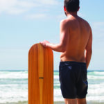 Chris stands with the otter surfboards wooden bellyboard in his Riz Boardshorts