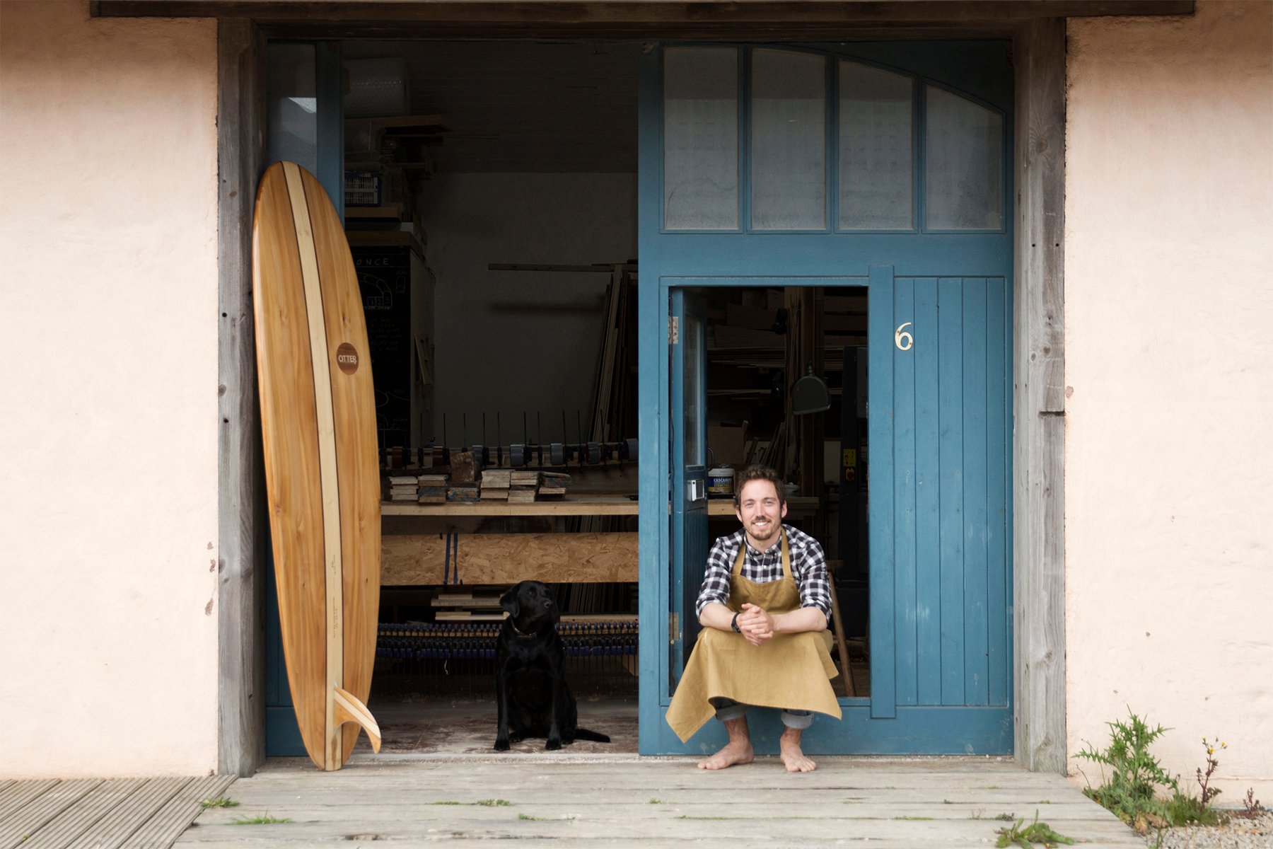 James Otter Wooden surfboard maker in his workshop in Cornwall with his dog, buddy