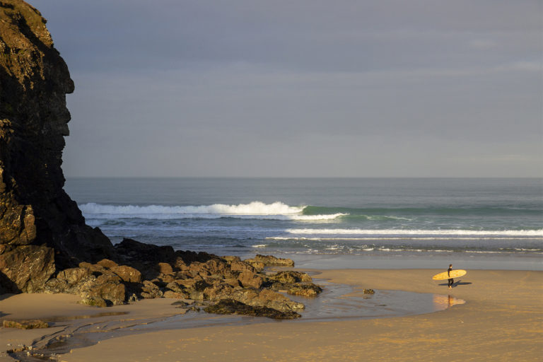 James Otter with his Pieces of Eight wooden surfboard exiting the surf at Chapel Porth, Cornwall.