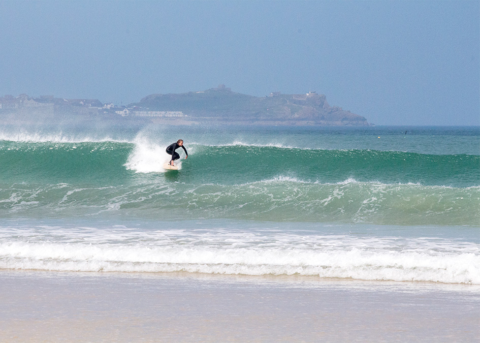 Sophie Hellyer on the beach in wetsuit with otter wooden surfboard coaster surfing with st ives in background