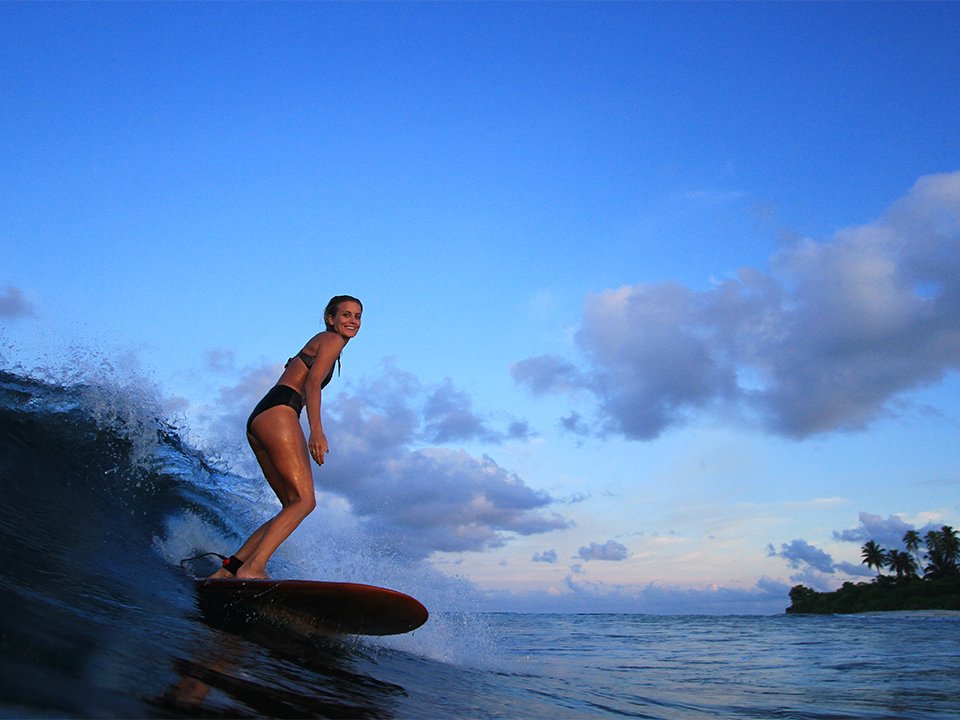 Sophie Hellyer on the beach in wetsuit with otter wooden surfboard in maldives seadar