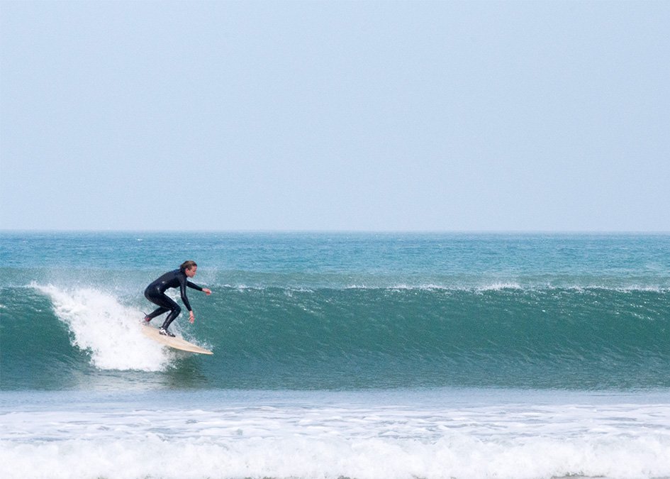 Sophie Hellyer on the beach in wetsuit with otter wooden surfboard coaster surfing