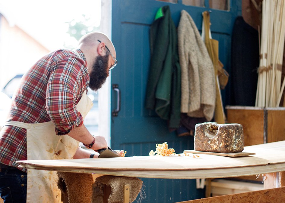 Stuart planing the rails of his wooden surfboard in the otter workshop cornwall