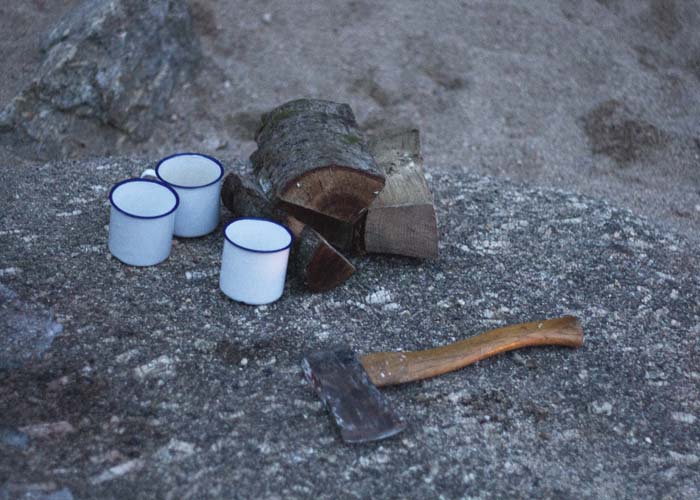axe with enamel mugs and wood on the beach