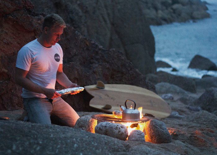 sean cooking on fire with wooden surfboard on the beach