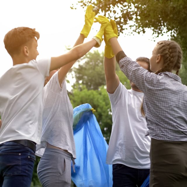 Team of volunteers hi-fiving during collecting garbage in park, save nature