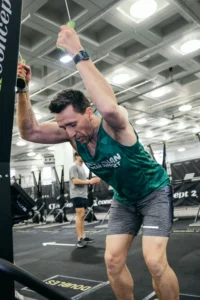 Athlete mid-stroke on SkiErg, strong downward pull, sweat visible, modern gym