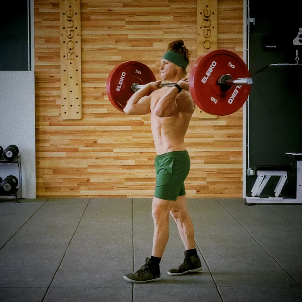 Athlete performing barbell front rack carry, elbows high, bar across shoulders, walking forward with upright posture, cinematic gym lighting showing composure and core strength
