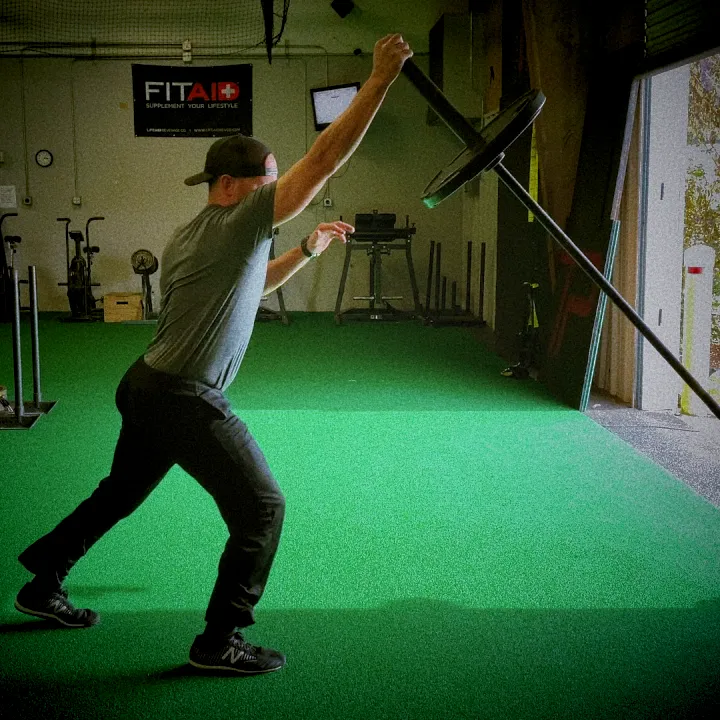 Athlete performing landmine split jerk, barbell angled upward, split stance mid-catch, cinematic gym lighting