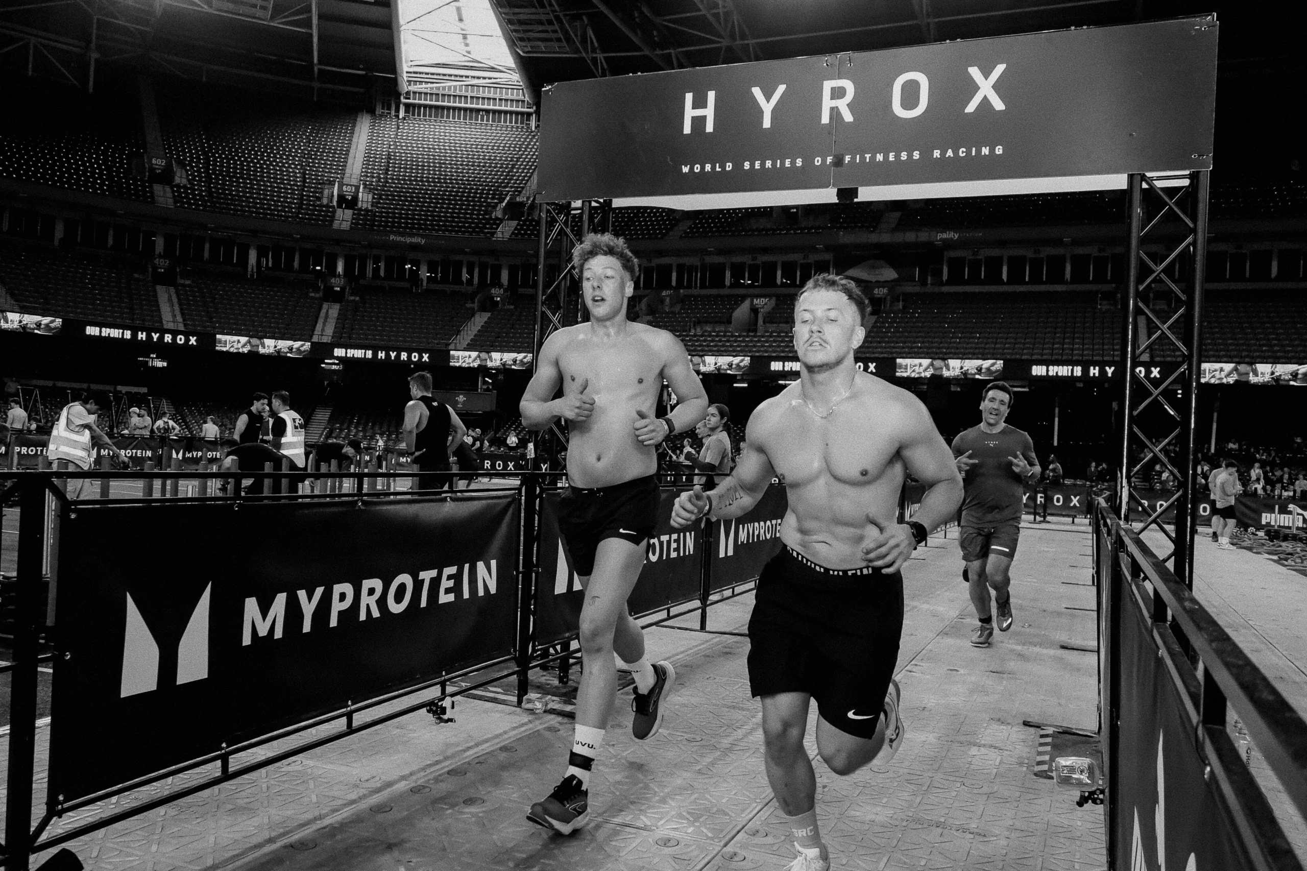 Athlete mid-race transitioning between running and sled push, HYROX arena lighting