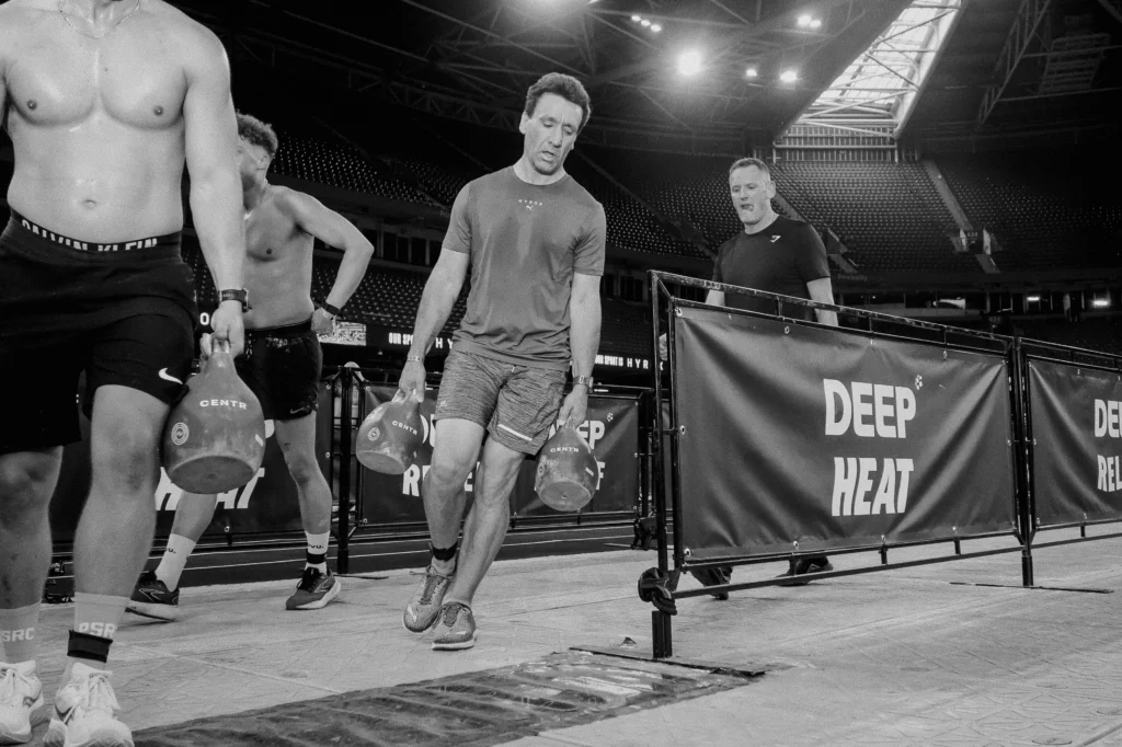 Athletes performing farmers carry at HYROX cardiff, cinematic black and white