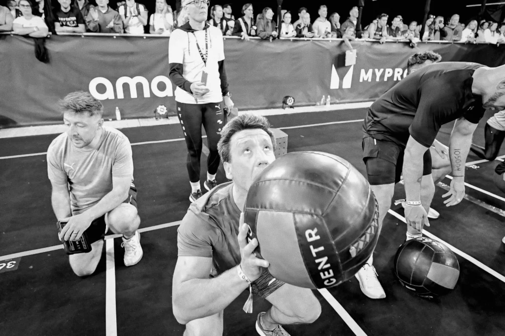 Athlete mid-wall-ball throw under spotlights, blurred spectators