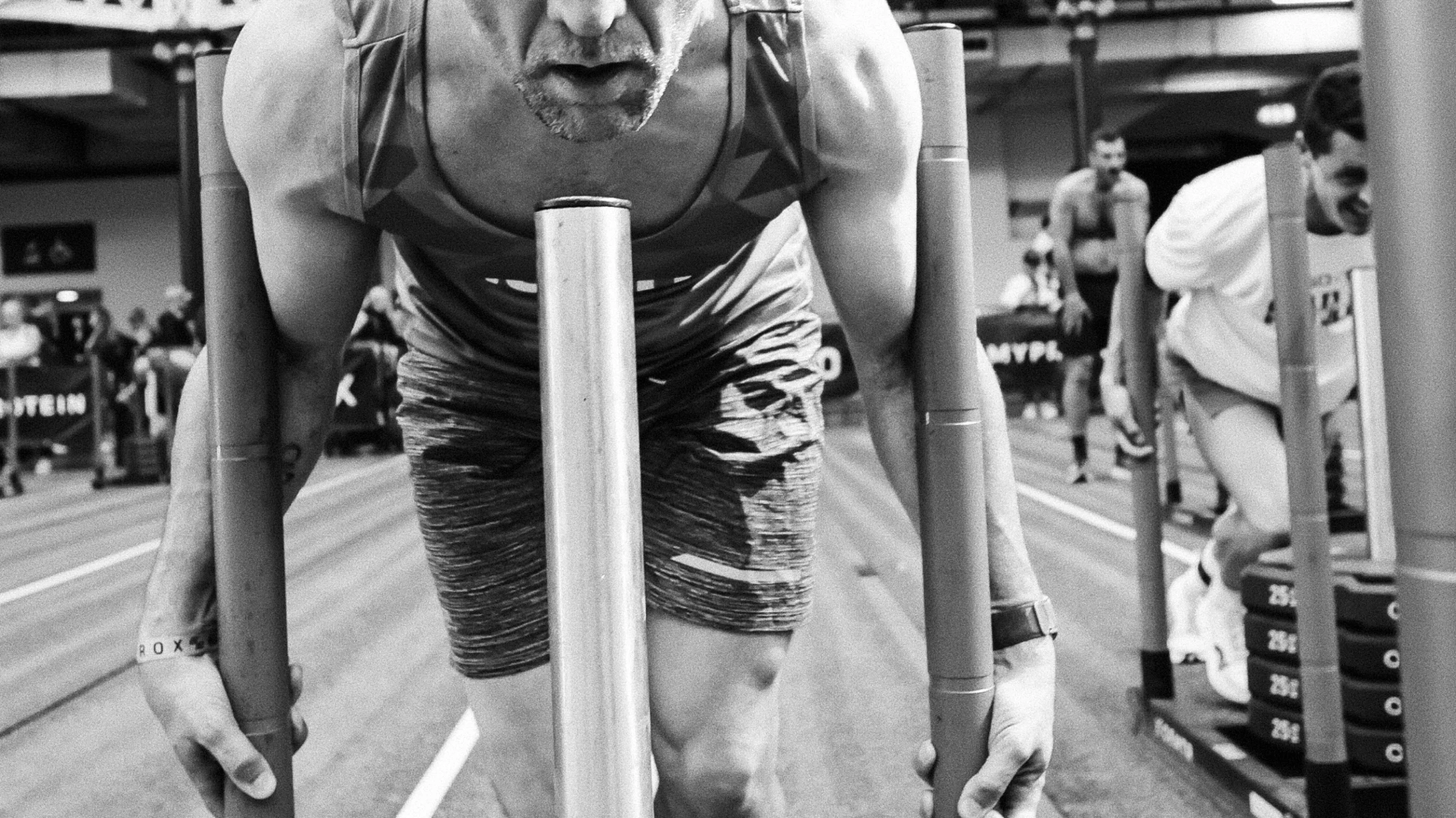 Athlete mid-sled push at London Olympia, sweat and motion visible
