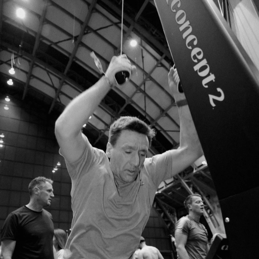 Athlete training on SkiErg in an industrial gym, mid-pull with visible timer overhead