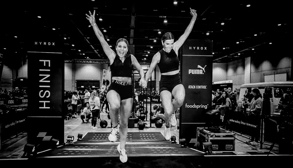 Athlete crossing HYROX finish line, exhausted and elated, crowd cheering