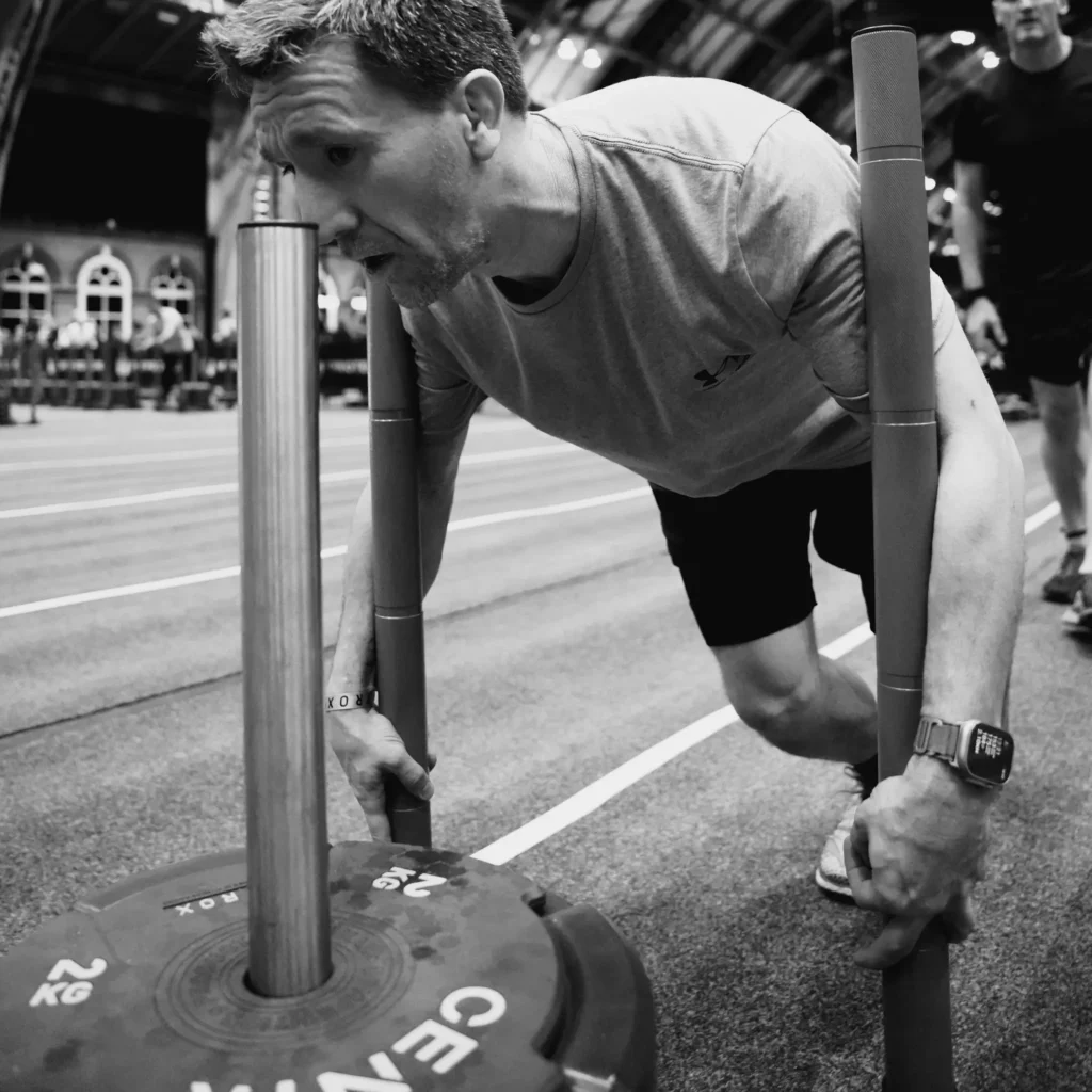 Athlete leaning low into loaded sled, head down, upper arms on upright poles