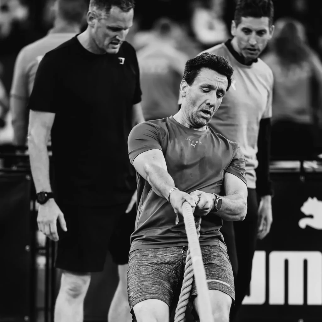 Athlete mid-sled pull using thick rope, leaning back with tension through arms and legs