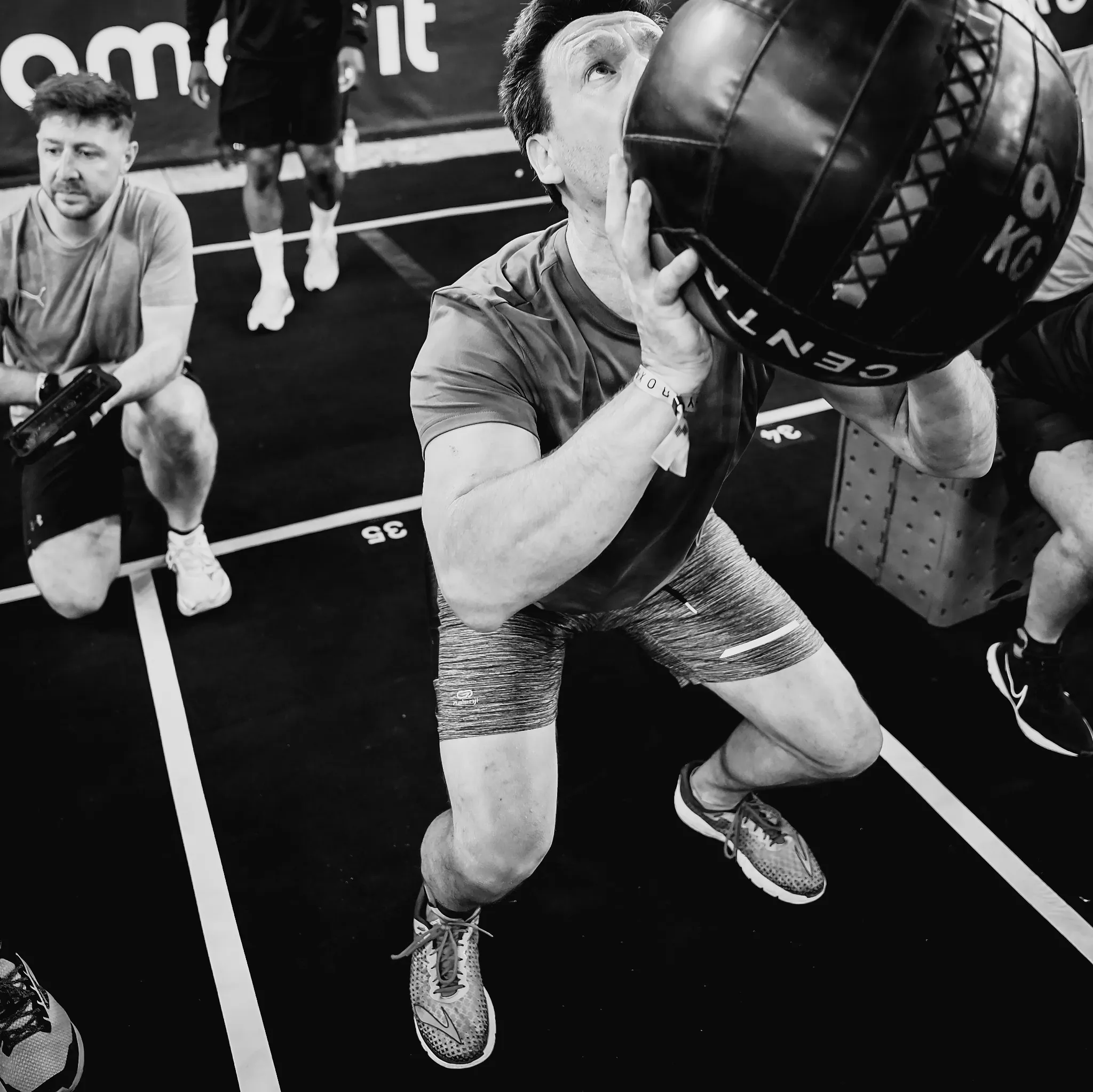 Athlete mid-wall-ball throw under bright gym lighting