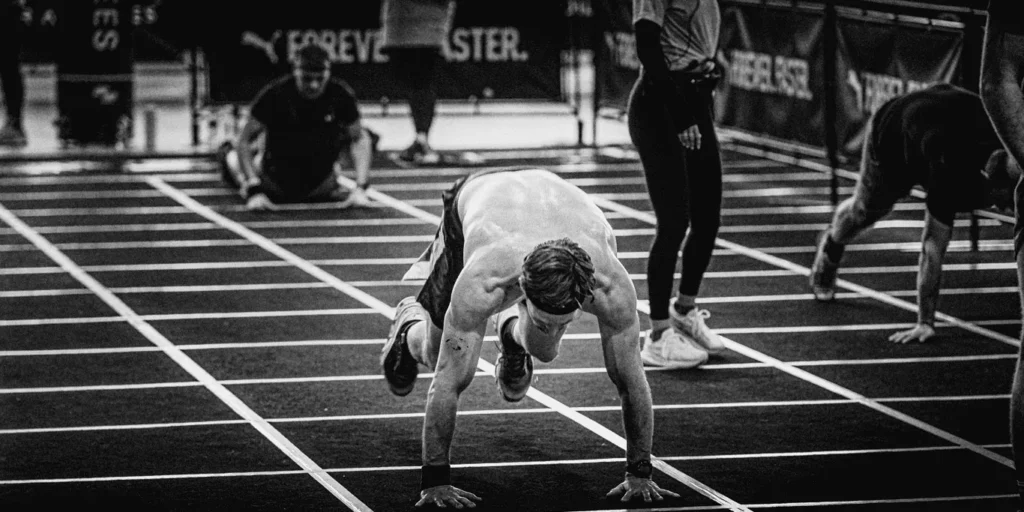 Athlete performing burpee broad jump mid-air, hands forward, legs extended