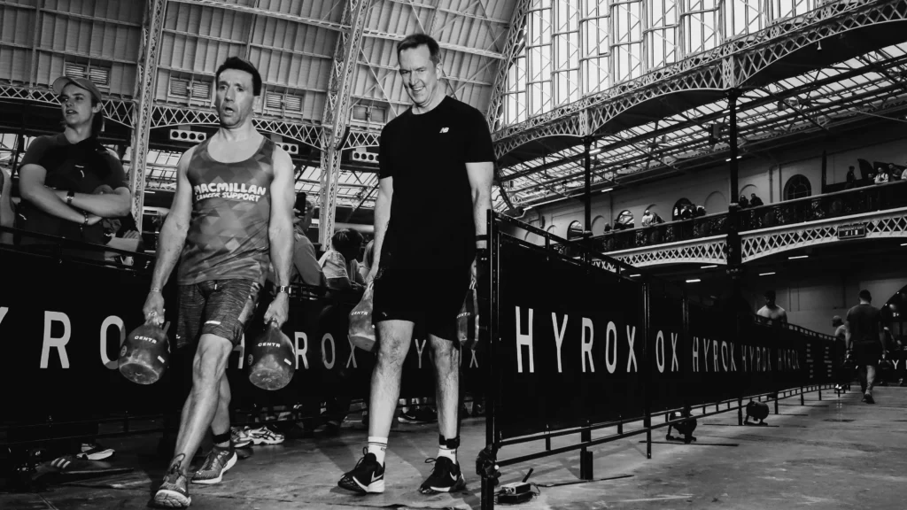 Athlete walking mid-carry, shoulders retracted, kettlebells stable by sides