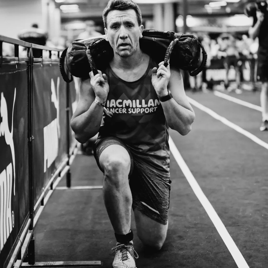 Athlete stepping forward in deep lunge with sandbag across shoulders, neutral spine
