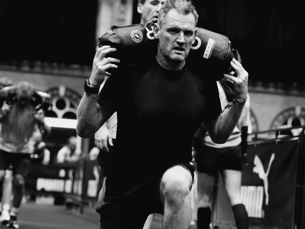 Close-up of athlete’s core and posture during lunge, showing sandbag placement and shoulder tension