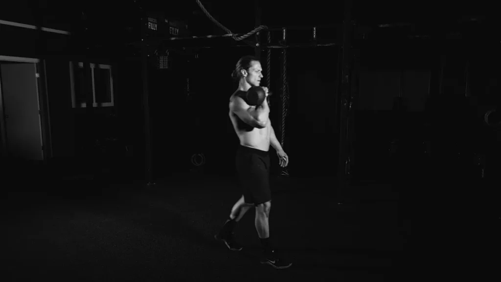 Athlete performing single-arm kettlebell carry, tall posture, visible core engagement
