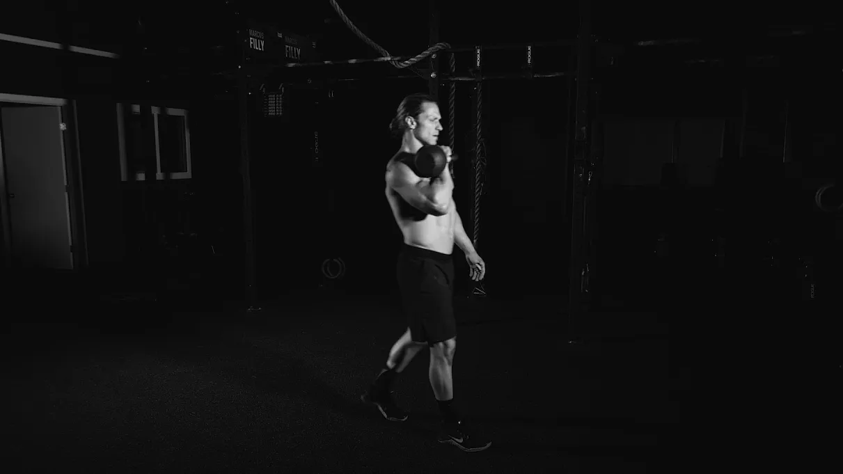 Athlete performing single-arm kettlebell carry, tall posture, visible core engagement