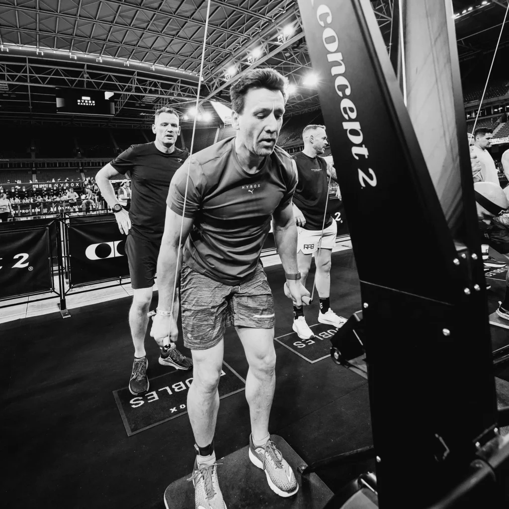 Athlete mid-SkiErg pull under HYROX signage, powerful stance and control