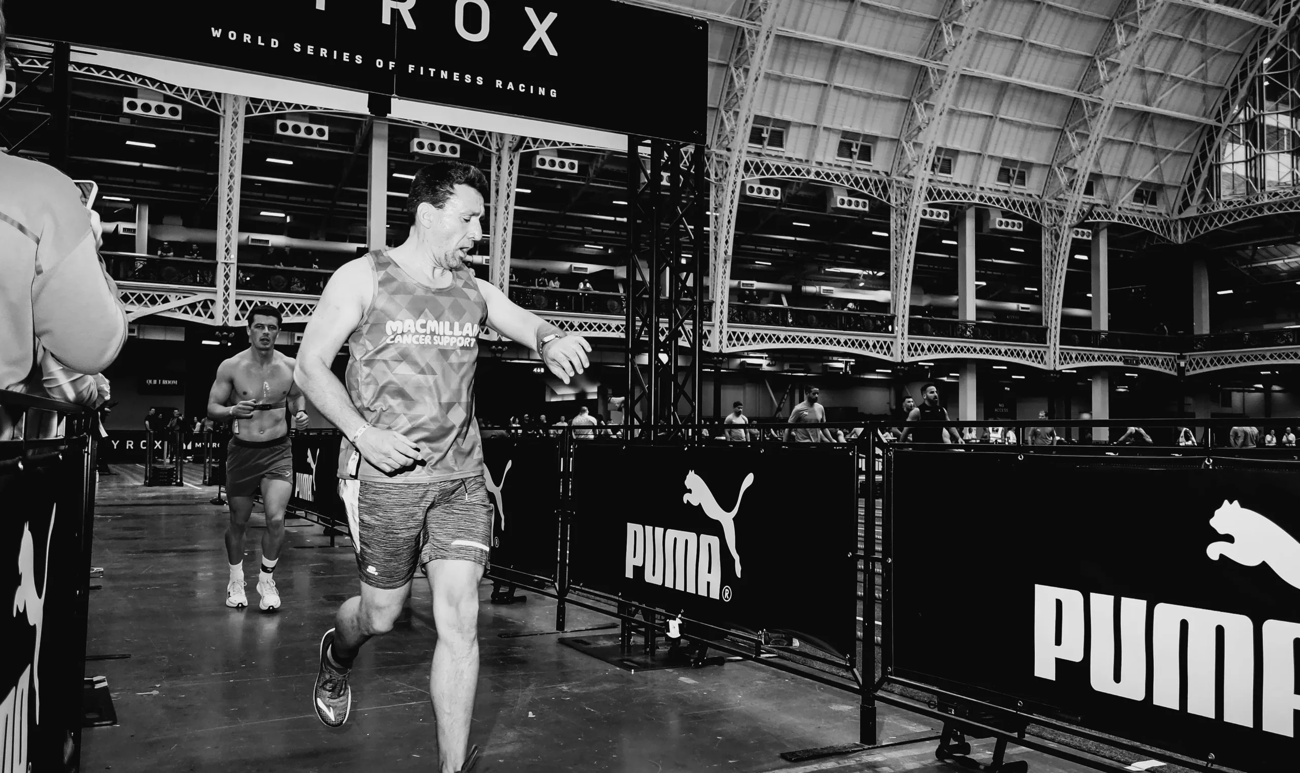 Athlete running past HYROX station lanes mid-race, steady stride and relaxed face