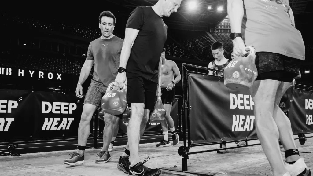 Two HYROX athletes tagging mid farmers carry station