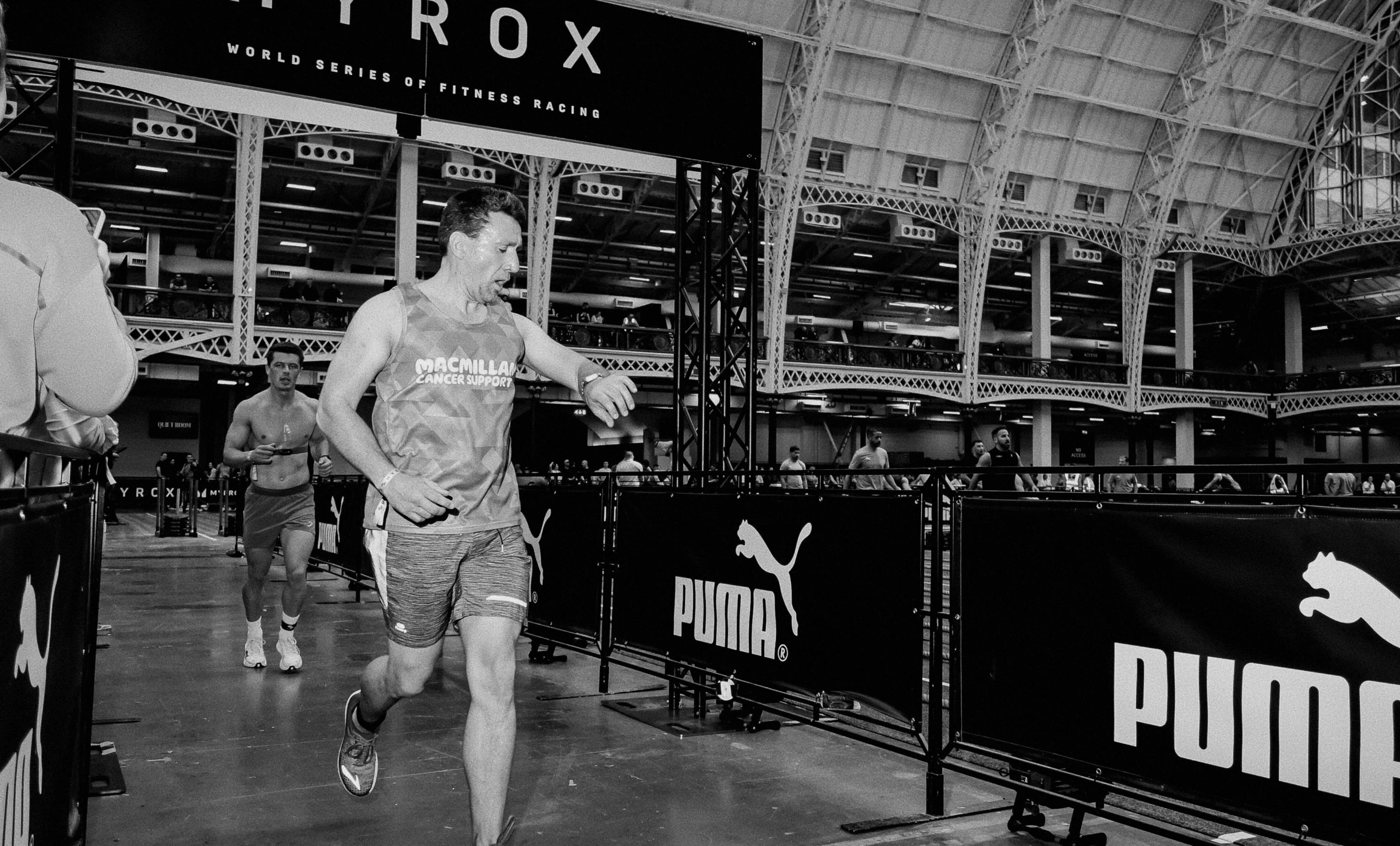 Athlete mid-run in HYROX arena, checking pace with a focused expression