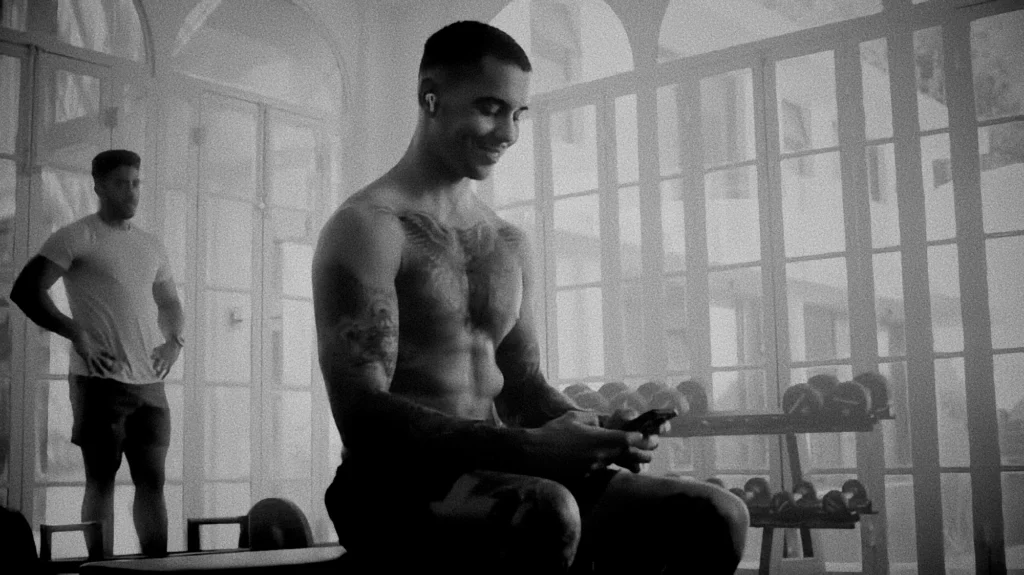 man on his phone sitting on a bench in a gym