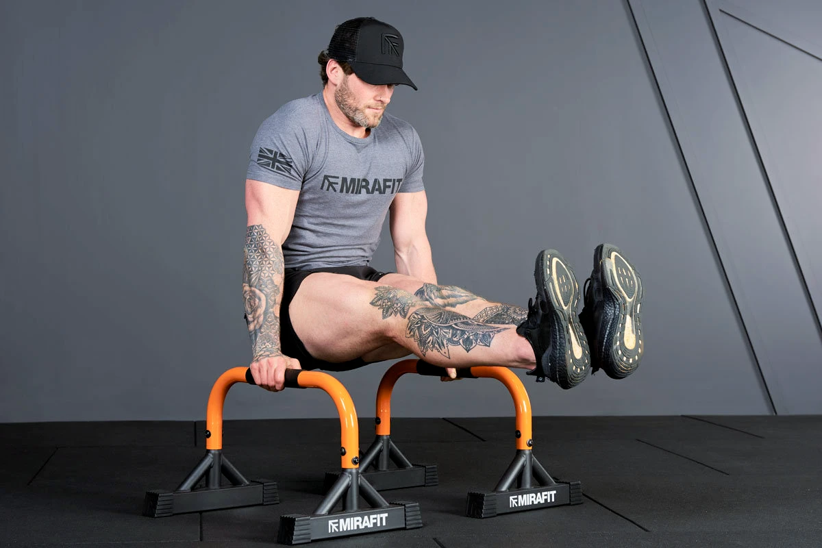 Athlete holding an L-sit on parallel bars in a dark industrial gym