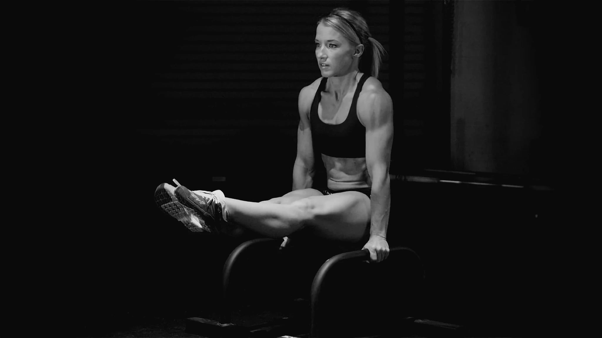 athlete performing L-sit hold, gym flooring and shadows in background