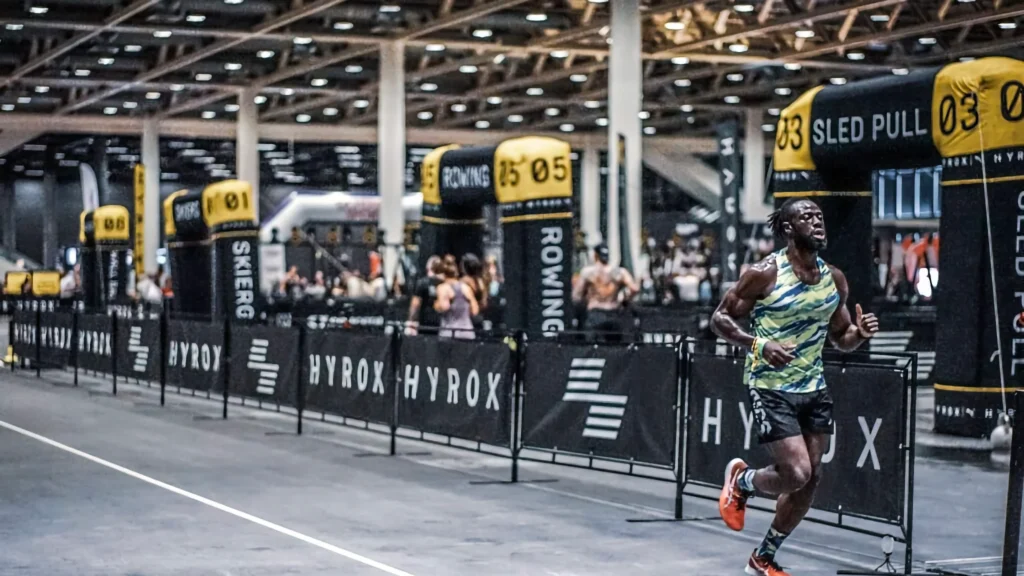 Athlete running through wide indoor straight with HYROX barriers