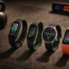Four sleek fitness bands arranged on a dark rubber gym floor beside a kettlebell and interval timer