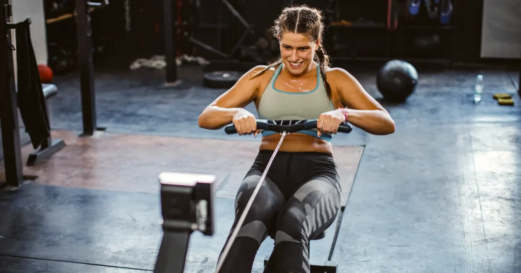 Athlete rowing at moderate pace, relaxed shoulders, consistent stroke rhythm. PM monitor visible showing steady calorie accumulation