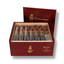 Open burgundy wooden presentation box of 21 Crowned Heads Broadway Robusto Extra cigars, showing individually sleeved dark brown cigars with ornate red and gold Crowned Heads bands, separate Broadway bands and navy-blue foot ribbons.