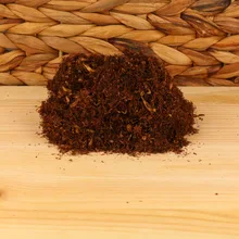 A small pile of dark hand rolling tobacco on a wicker and wood background